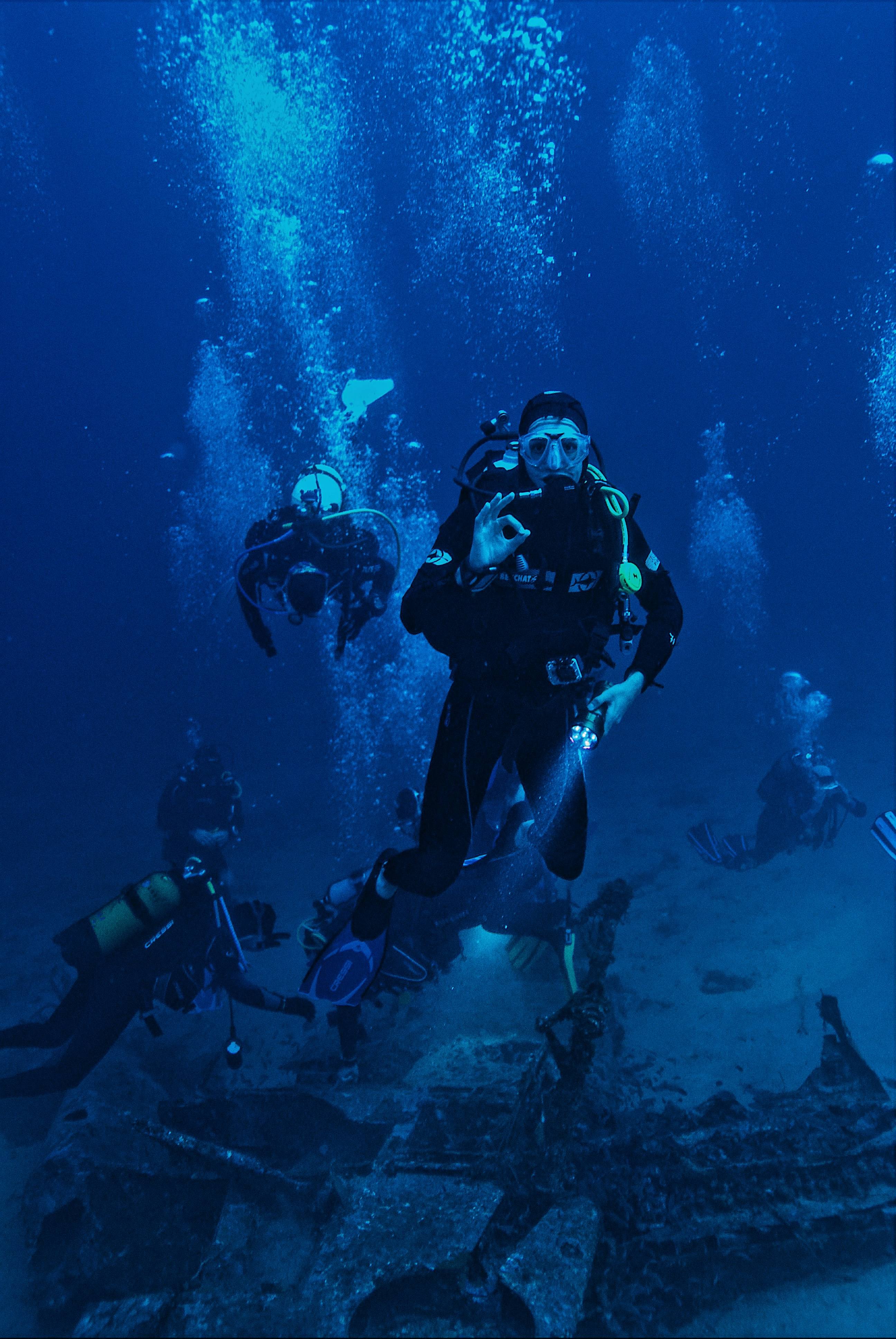 A diver signalling OK at depth, bubble columns rising, other divers in the background